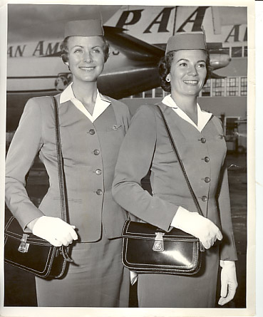1950s Two Pan Am Stewardesses in full uniform of the era show their white smiles & gloves with a Boeing 377 Stratocruiser in the background.